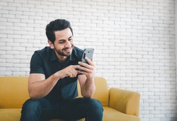 man sitting on yellow sofa using smartphone with smiling face, lifestyle concept