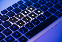 Fake news written on a backlit laptop keyboard close-up with selective focus in a blue ambiant light