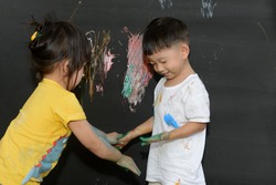 Cute little asian boy and girl enjoying arts and crafts painting with  hands on the blackboard