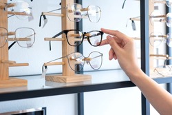Hand of  woman choosing the glasses in optics store, eyesight and vision concept 