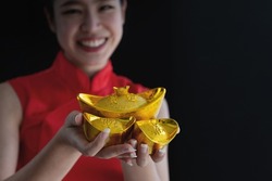 Chinese girl wears traditional dress holds Chinese gold ingots on black background, represents wealth and prosperity, Chinese text language means wealth and prosperity, Chinese new year concept