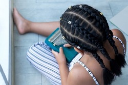African girl with braided hair   playing wooden Kalimba instrument on floor, Kalimba or Thumb Piano acoustic music instrument from Africa, view from above