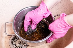 above view of gloved hands scrub stewpan with burnt food with metal sponge in pink sink at home kitchen