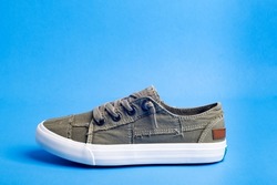 One green casual canvas shoe on a blue background. Space for text.