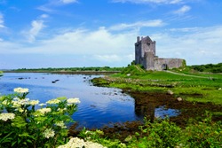 View of the medieval Dunguaire Castle along the shore of Galway Bay with reflections and flowers, Ireland