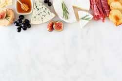 Assorted cheeses and meat appetizers. Top border, overhead view on a white marble background with copy space.