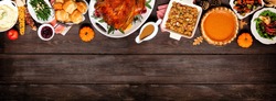 Traditional Thanksgiving turkey dinner. Above view top border on a dark wood banner background with copy space. Turkey, mashed potatoes, dressing, pumpkin pie and sides.