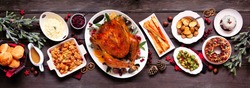 Traditional Christmas turkey dinner. Top view panoramic table scene on a dark wood banner background. Turkey, potatoes and sides, stuffing, fruit cake and plum pudding.