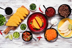 Taco bar table scene with a variety of ingredients. Above view on a rustic white wood background. Mexican food buffet.