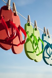 Red, green and blue flip-flops hanging on a line with a sky background