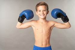 Cheerful boy in boxing gloves standing against gray background