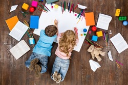 Happy children. Top view creative photo of little boy and girl on vintage brown wooden floor. Children lying near books and toys, and painting