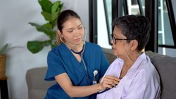 The old woman was cared for by her caregiver. Nurse or Doctor visiting senior woman for check-Up. Uses a stethoscope to listen to the heartbeat of an elderly woman at home.