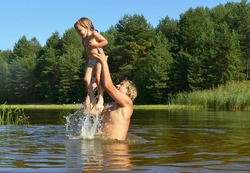 In the summer, bright sunny day, the little girl and man is bathed dives,run, jumps into the river. Beside him spray. 