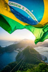 Brazilian flag shines above the golden sunset city skyline at Sugarloaf  Mountain in Rio de Janeiro Brazil. Translation: Order and Progress