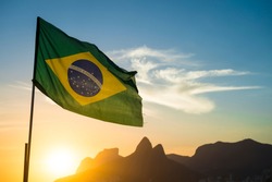Brazilian flag waving backlit in front of the golden sunset mountain skyline at Ipanema Beach in Rio de Janeiro, Brazil