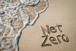 Net Zero message for energy consumption handwritten on smooth sand beach with oncoming wave 