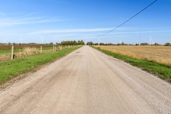 Empty straight unpaved countryroad through farmland dotted with wind turbines on a clear autumn day