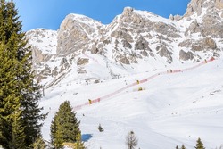 Chairlifts and ski runs at the foot of  towering snowy rocky peaks in the Alps on a sunny winter day