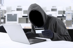 Internet Theft - a man wearing a balaclava and holding a credit card while sat behind a laptop, 