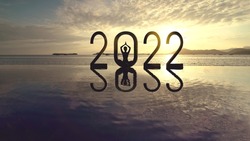 Silhouette of young woman meditating with 2022 numbers on the beach at sunset time