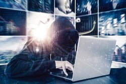 Double exposure of hooded hacker using a laptop while sitting with blurred virtual screen background