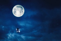 Rear view of little girl sitting alone on the swing while hanging on the moon at nighttime