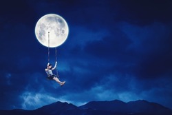 Happy young woman sitting on the swing while hanging on the moon at nighttime