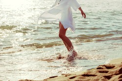barefoot woman enjoy in sea water in white long shirt, lower body,  side view