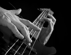 male fingers playing on electrical bass guitar, black and white
