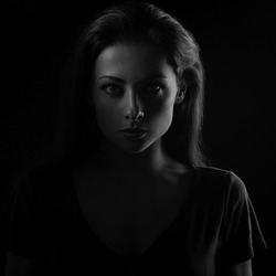 Beautiful serious mysterious woman in darkness looking dramatic. Closeup portrait in dark shadow low key. Art.  closeup front face view on black background. Black and white
