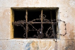 Old stonemade window with bars and barbed-wire on it