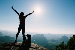 Successful woman hiker open arms at the sunrise mountain top cliff edge