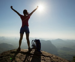 Silhouette of free cheering woman hiker open arms at mountain  top cliff edge