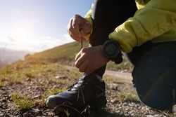Woman trail runner tying shoelace while cross country running  on mountain top