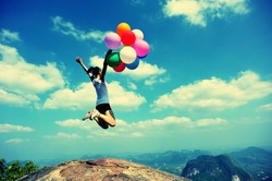 young asian woman jumping on mountain peak rock with colored balloons 