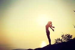 cheering woman open arms at sunset mountain top cliff edge