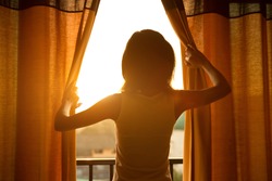 Young woman stand in the room opening curtain seeing the beautiful sunrise