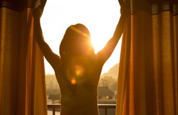 Young woman stand in the room opening curtain seeing the beautiful sunrise