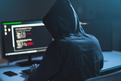 cybercrime, hacking and technology concept - male hacker in dark room writing code or using computer virus program for cyber attack