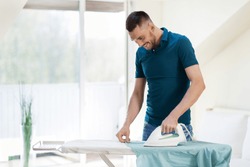 housework and household concept - man ironing shirt on iron board at home