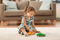 childhood and people concept - happy three years old baby girl playing with toy car at home
