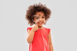 investigation, discovery and vision concept - happy little african american girl looking through magnifying glass over grey background
