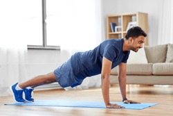 fitness, sport, training and concept - indian man doing push ups at home