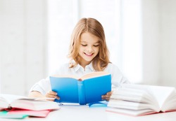 education and school concept - little student girl studying and reading book at school