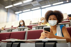 education, healthcare and pandemic concept - african student girl wearing face protective medical mask for protection from virus disease with smartphone at lecture