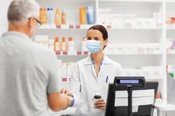 medicine, pharmaceutics, health care and people concept - apothecary wearing face protective medical mask for protection from virus disease and senior man customer buying drug at drugstore