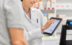 medicine, pharmaceutics, healthcare and technology concept - close up of smiling female pharmacist showing digital prescription on tablet pc computer to customer at pharmacy