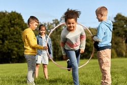 childhood, leisure and people concept - group of happy children playing game with hula hoop at park