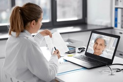 healthcare, technology and medicine concept - female doctor in white coat with laptop computer and cardiogram having video call with patient at hospital